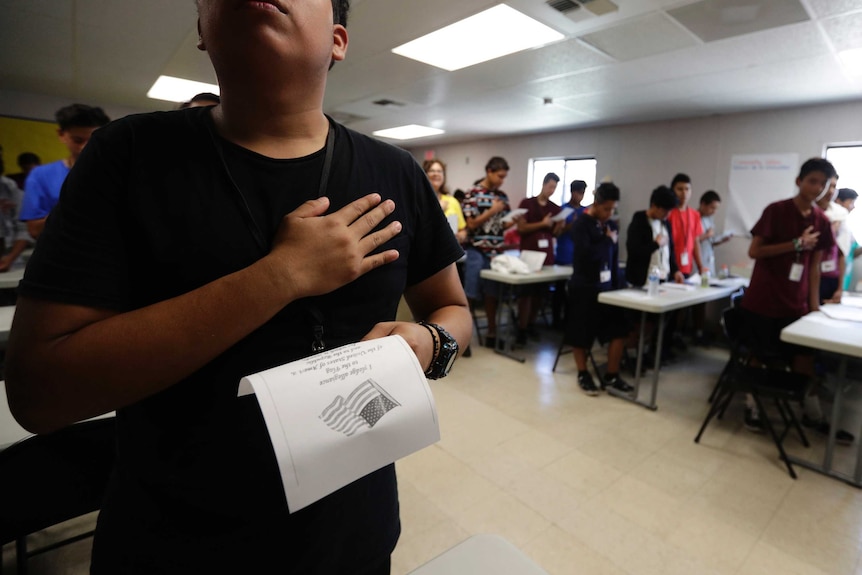 A boy with his hand on his heart holding a piece of paper with the US pledge of allegiance written on it