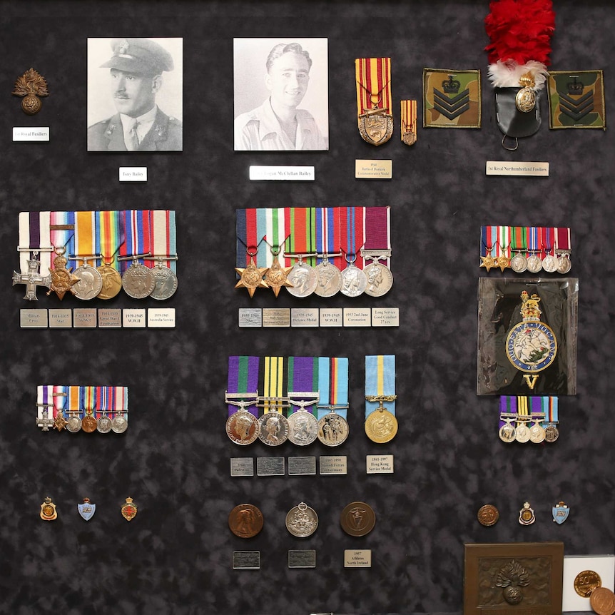 War medals and old photos of Peter Bailey on display in a framed cabinet hanging on a wall.