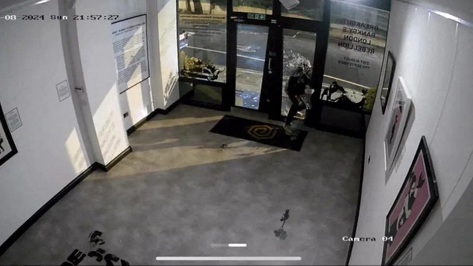 A CCTV image of a robber breaking into a gallery with a hammer.