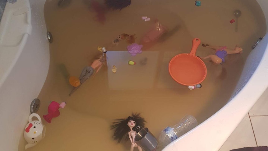 A bathtub full of brown water, with toys floating in it.