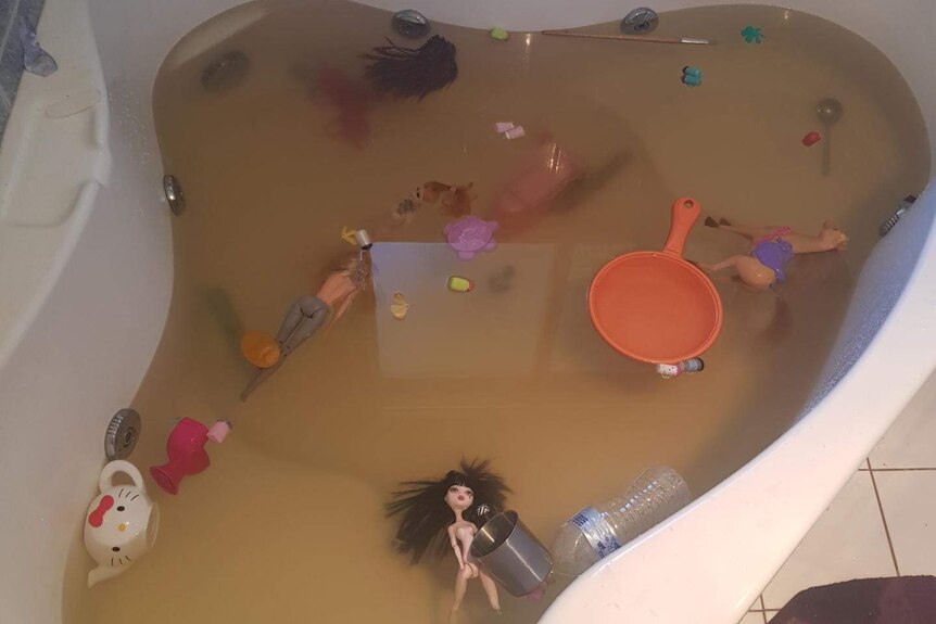 A bathtub full of brown water, with toys floating in it.