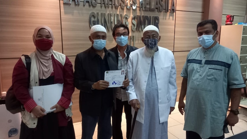 Abu Bakar Bashir, wearing white and a face mask, stands beside other people after his release from prison.