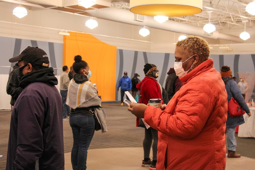 A woman waits in line while inspecting the ballot in her hands