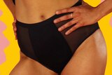 Woman wearing black period underwear with hand on hip, yellow and pink colours in background, to depict how period panties work.