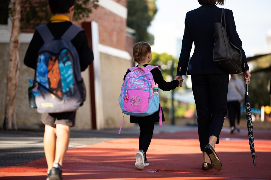 A girl with pink schoolbag on walks while holding her mum's hand.