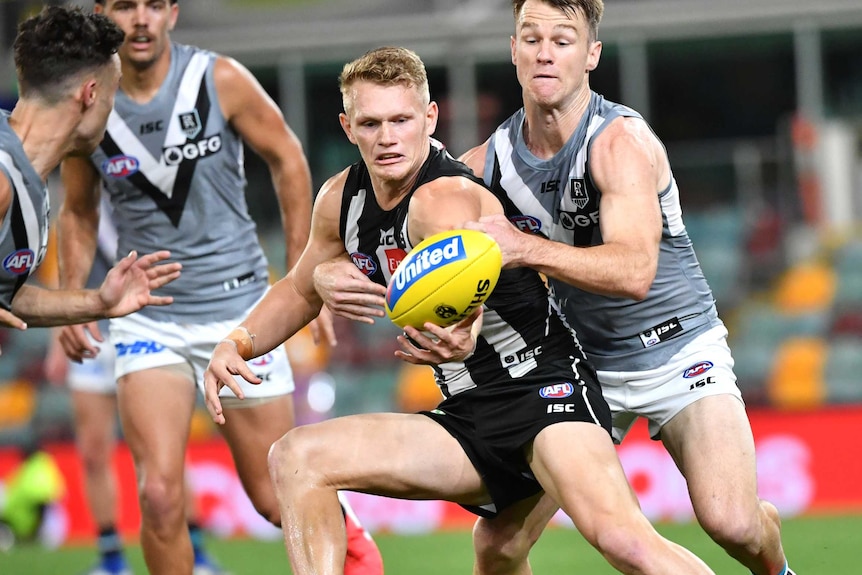 Adam Treloar fumbles the ball with one hand while under pressure from Robbie Gray
