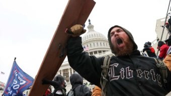 A man holding a shield yelling in anger with the capitol building visible in the background