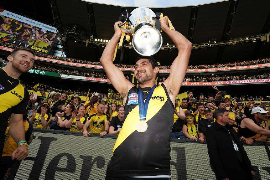Richmond Tigers player Marlion Pickett celebrates grand final win holding up cup smiling in front of crowd