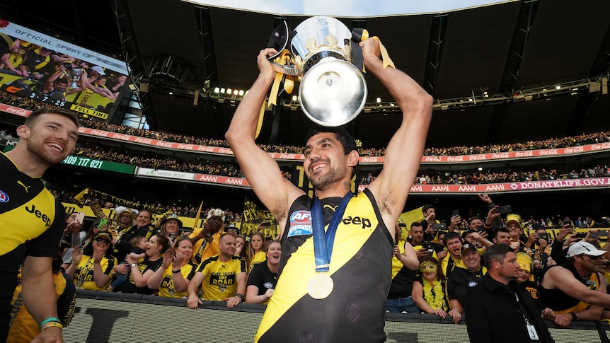 Richmond Tigers player Marlion Pickett celebrates grand final win holding up cup smiling in front of crowd