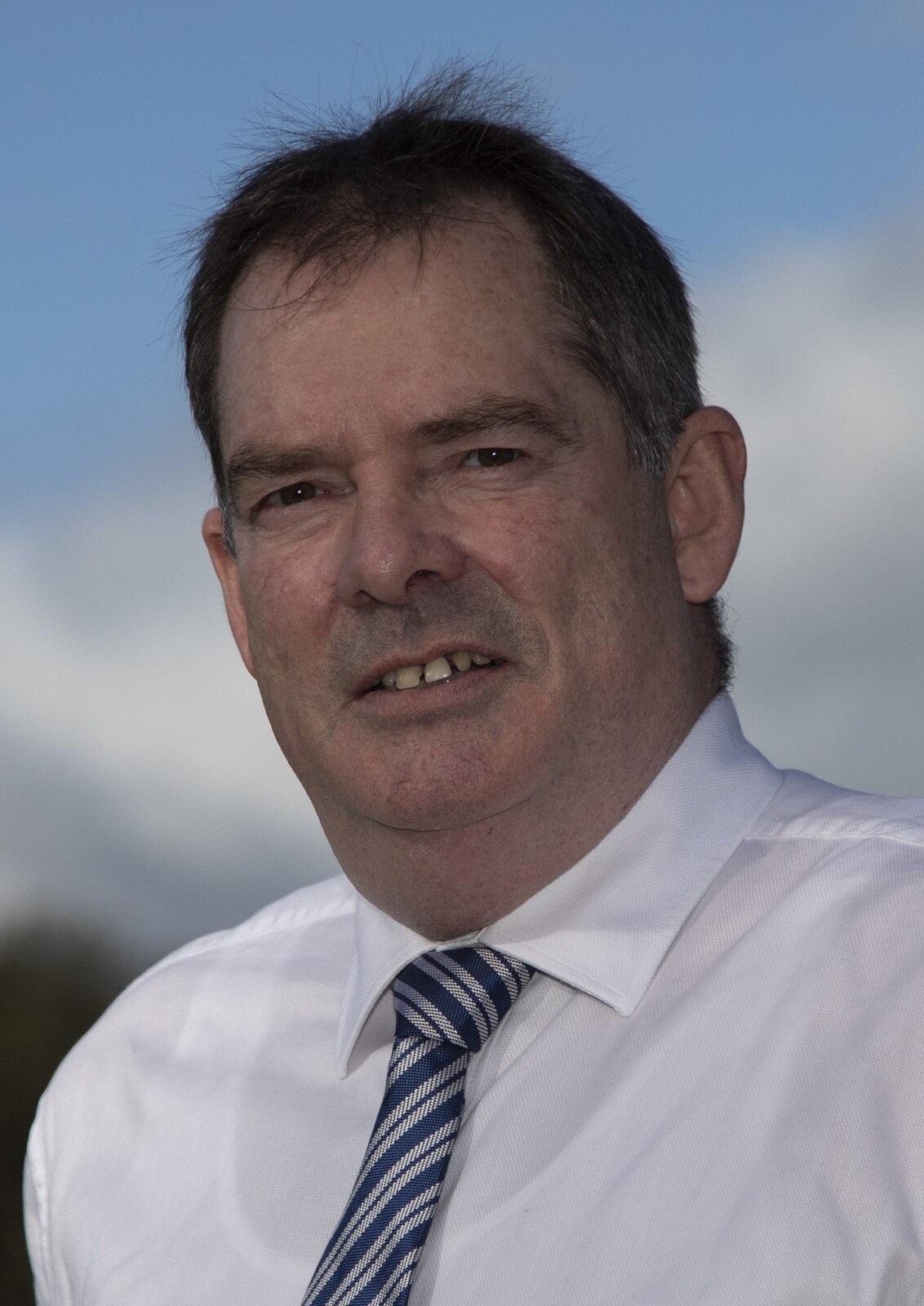 A man with short dark hair, wearing a crisp business shirt and tie.