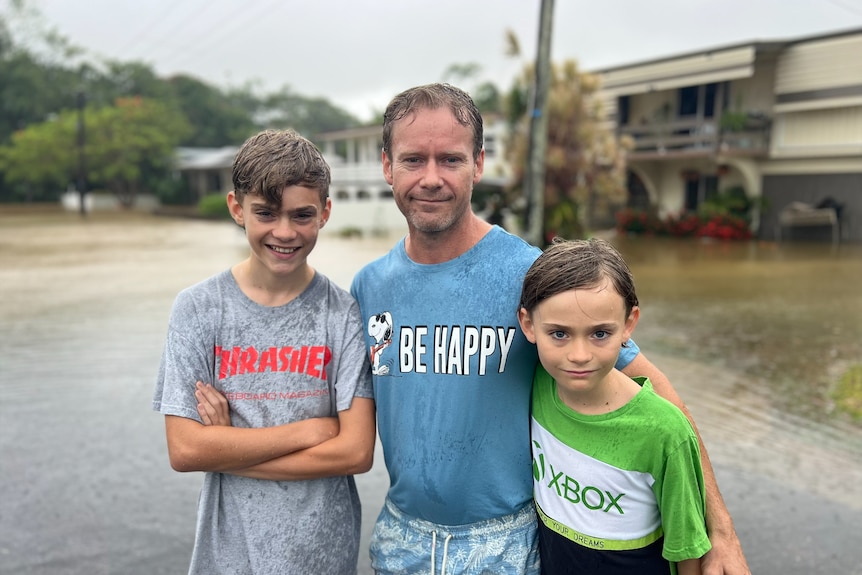 a man standing with flood waters behind, with his two boys