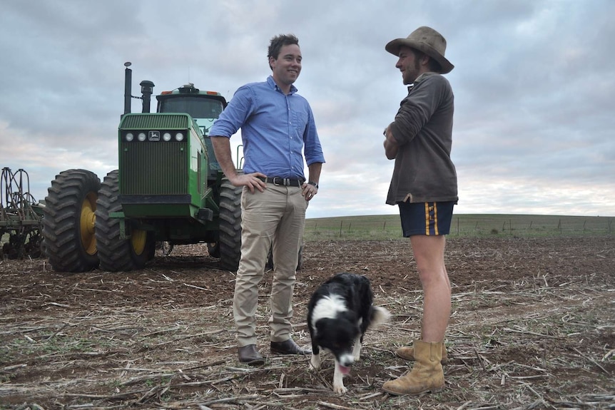 Two men stand talking in front of a tractor