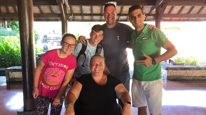 A family of four smiles while posing for a photo with another man. 