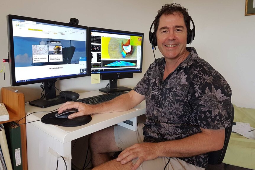 Man in a room with headphones in front of two computer screens