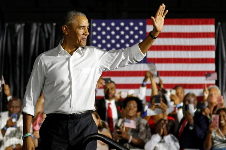 Barack Obama waves to the crowd with smile on his face as he leaves stage with American flag and excitable crowd in background