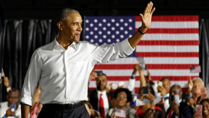 Barack Obama waves to the crowd with smile on his face as he leaves stage with American flag and excitable crowd in background