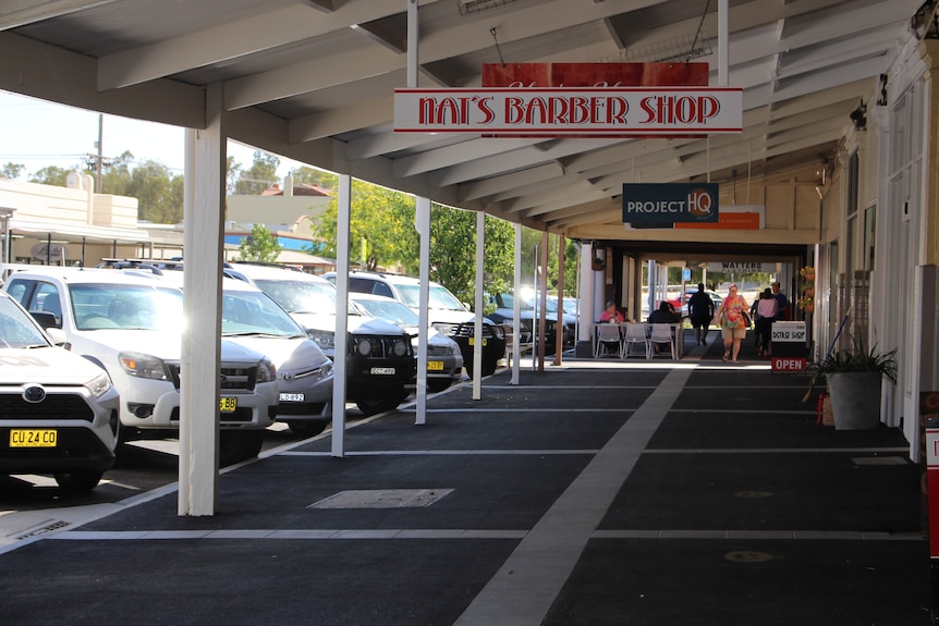 Footpath lined with cars parked front to curb. Awning over footpath, people in the distance.