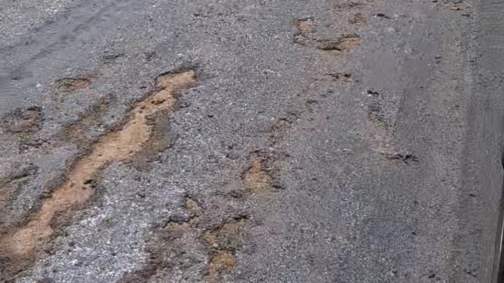 A long stretch of road showing bitumen cracking. The road is surrounded by vineyards