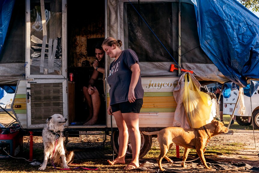 A man and woman outside a caravan with two dogs.