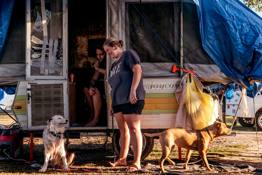 A man and woman outside a caravan with two dogs.