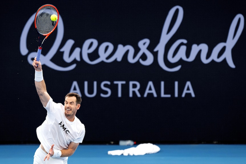 Andy Murray plays an overhand shot in a white outfit on court at the Brisbane International