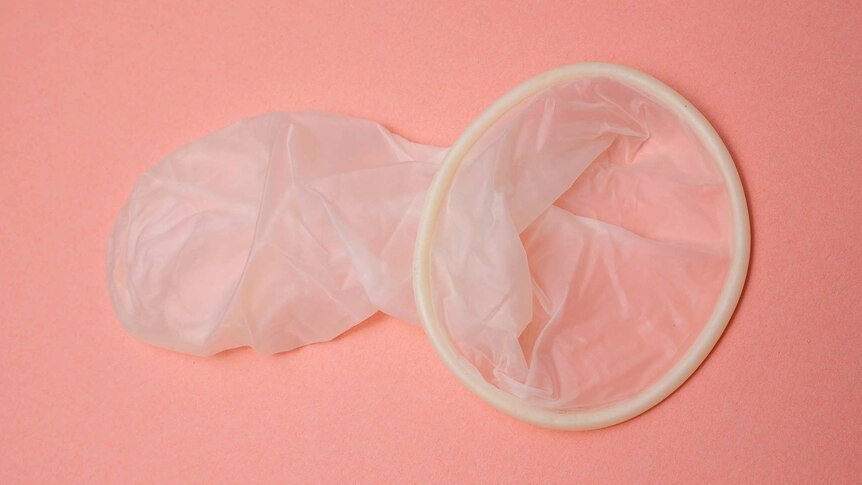 Unwrapped condom lays on pink background