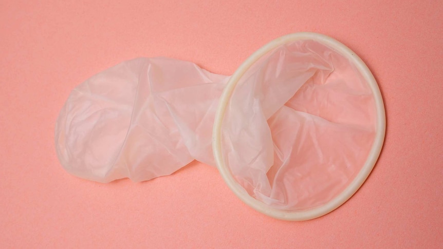 Unwrapped condom lays on pink background