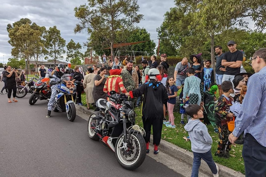 Costume-wearing clowns on motorbikes stop for photos with kids in a suburban street