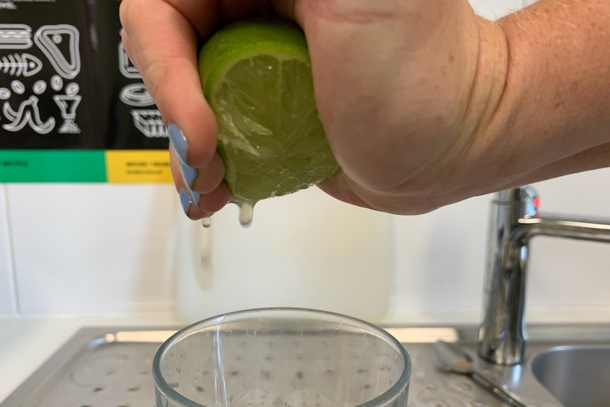 A hand squeezing juice from a lime.