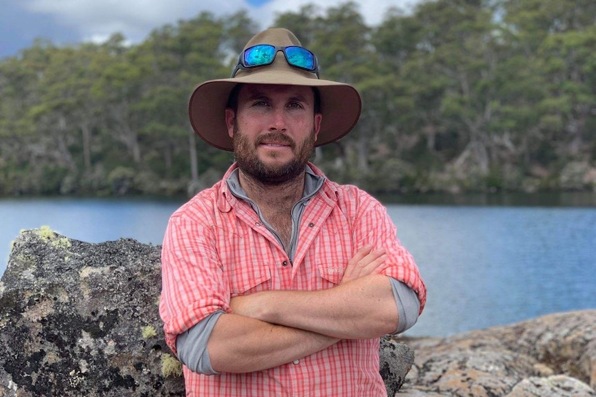 Daniel Hackett crosses his arms and stands in front of a lake.  He has a neutral expression