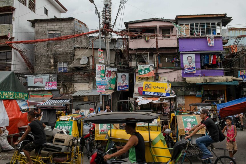 Dilapidated buildings on a street filled with bikes are covered in brightly coloured political posters