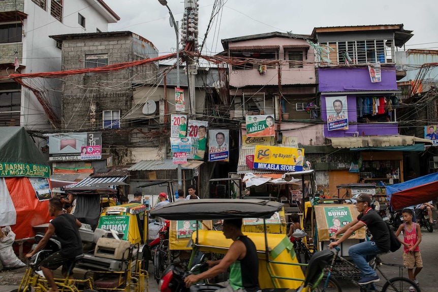 Dilapidated buildings on a street filled with bikes are covered in brightly coloured political posters
