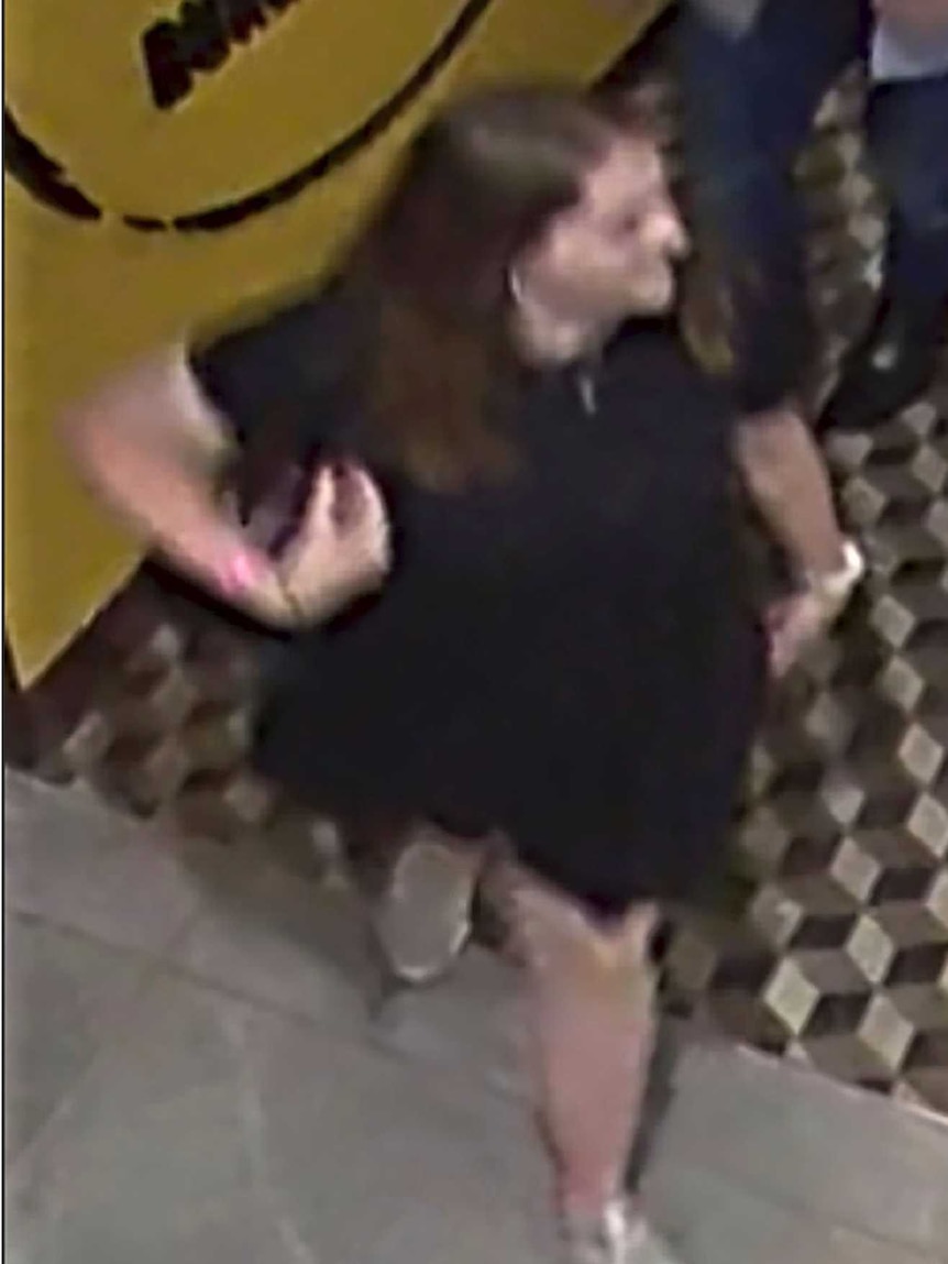 Grace Millane walks through a corridor in grainy CCTV footage. She is wearing a black dress, with white runners.