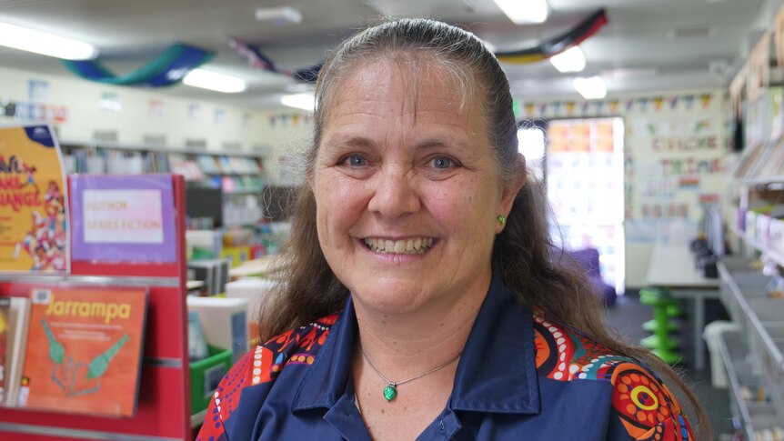 A portrait photo of a middle-aged woman with an colorful shirt in a library. 