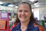 A portrait photo of a middle-aged woman with an colorful shirt in a library. 