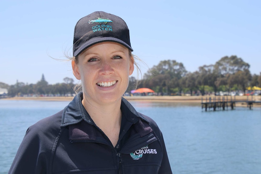 A head and shoulders shot of volunteer dolphin rescuer Natalie Goddard posing for a photo wearing a hat with a beach behind her.