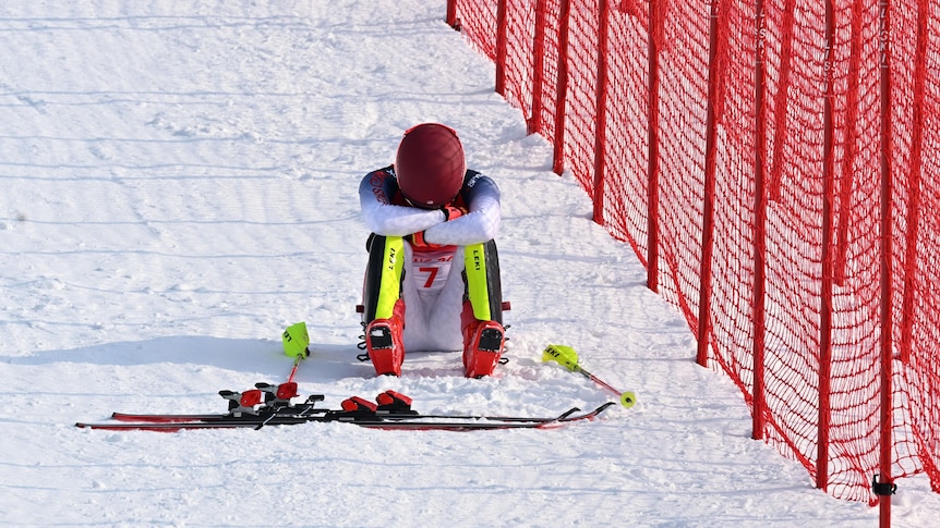 A winter athlete sits in the snow with their head in their arms