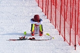 A winter athlete sits in the snow with their head in their arms