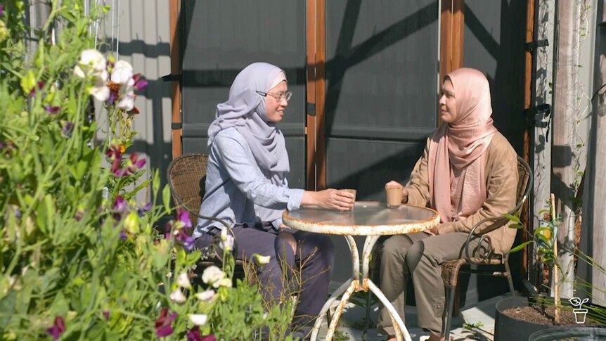 Two woman sitting at a table in a garden having a drink.