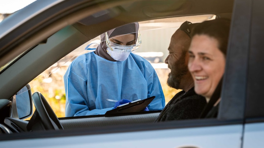 a person in PPE taking the details of a couple laughing a car