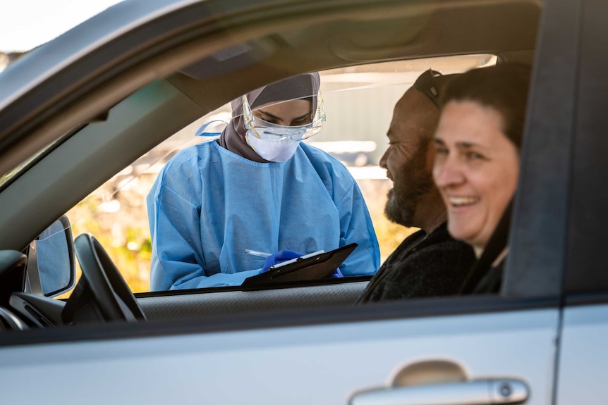 a person in PPE taking the details of a couple laughing a car