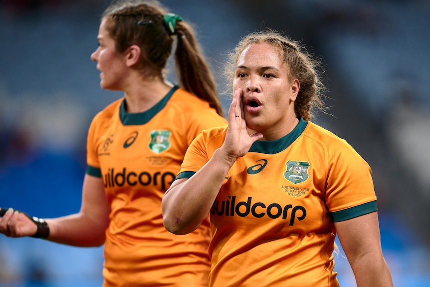 A Wallaroos player puts her right hand up close to her mouth as she speaks to a teammates.