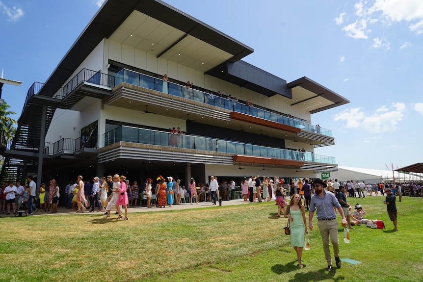 A three level grandstand with people milling about at the races. 