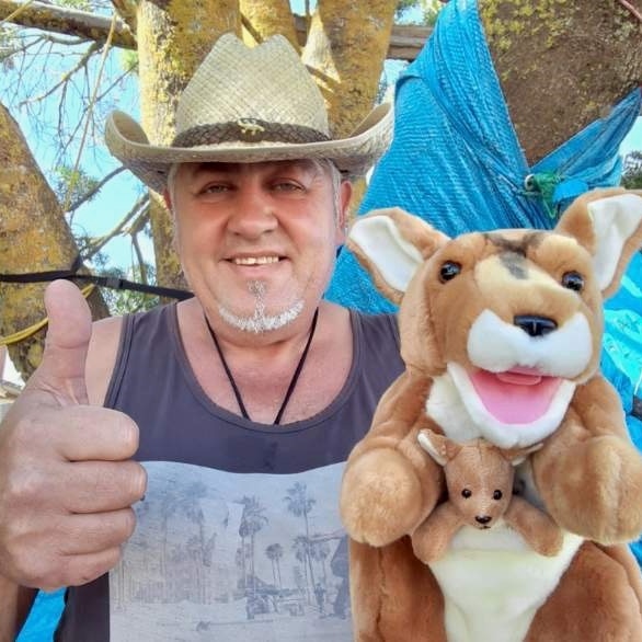 man in straw cowboy hat with grey goatee beard giving thumbs up with kangaroo puppet on other hand