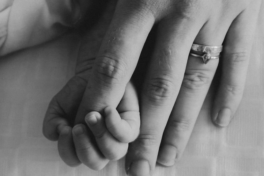 A close-up of  mother's hand, holding her newborn baby's hand.