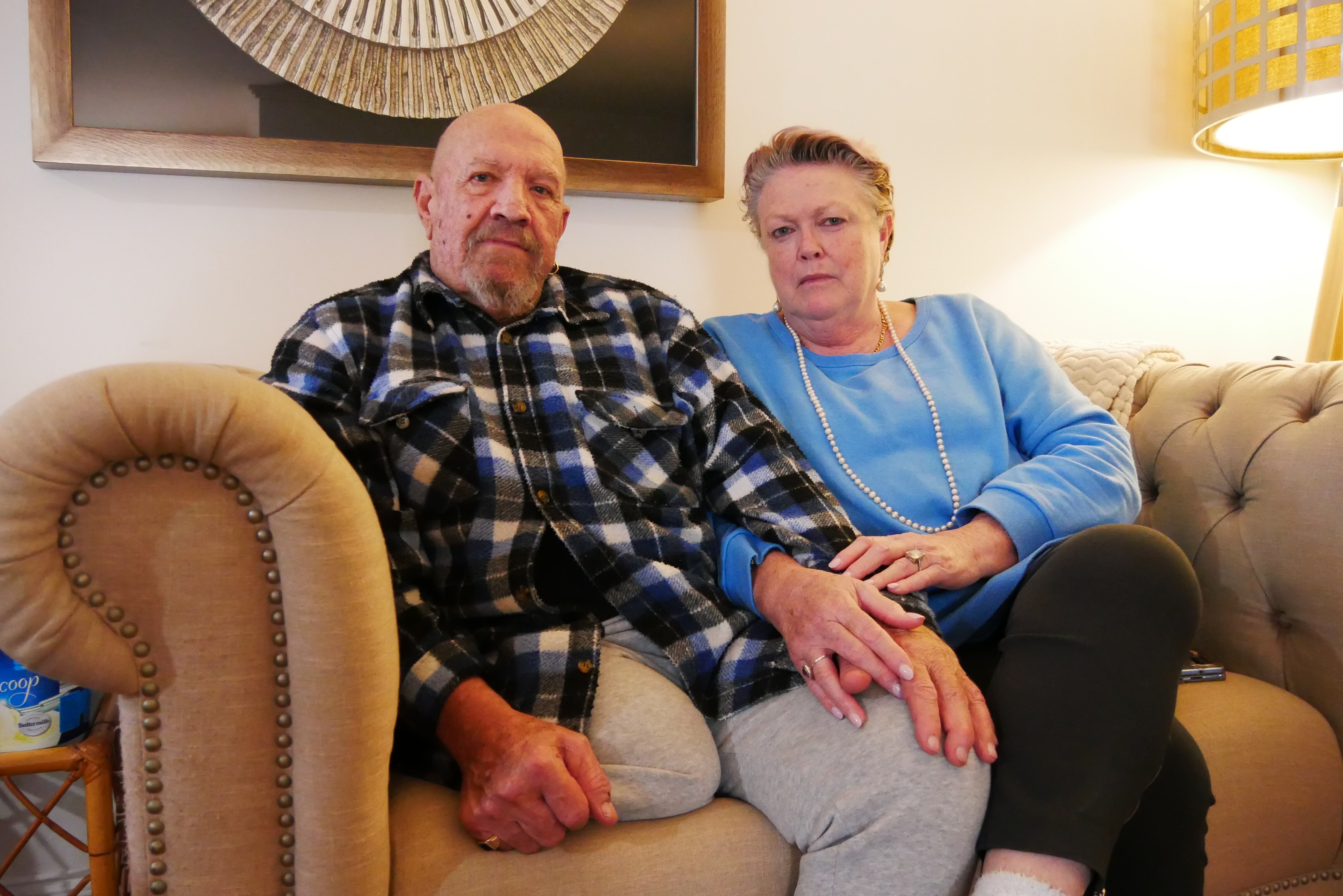 Two people sit on the couch looking serious. 