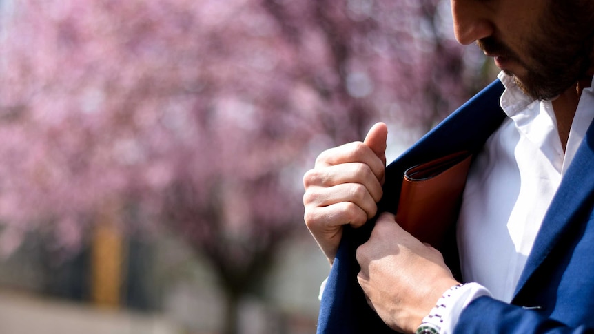 Man putting wallet into the inside pocket of his jacket, in front of pink background