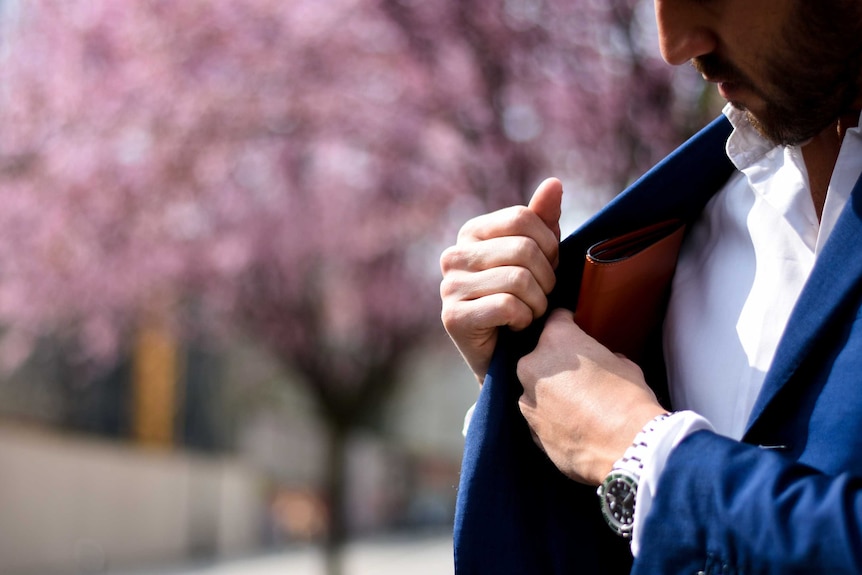 Man putting wallet into the inside pocket of his jacket, in front of pink background