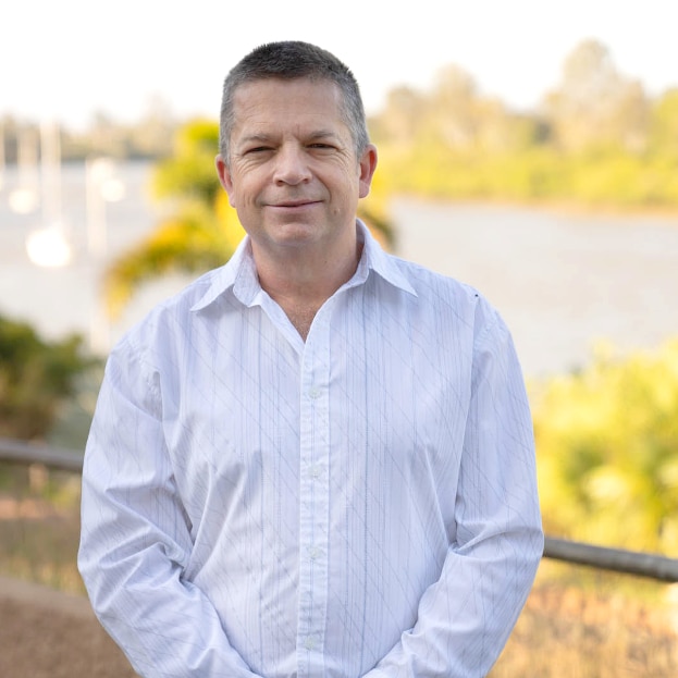 Man standing beside water in business shirt, gently smiling