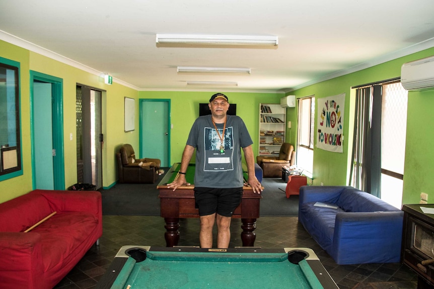 An Aboriginal man leaning on a pool table in an empty youth centre.